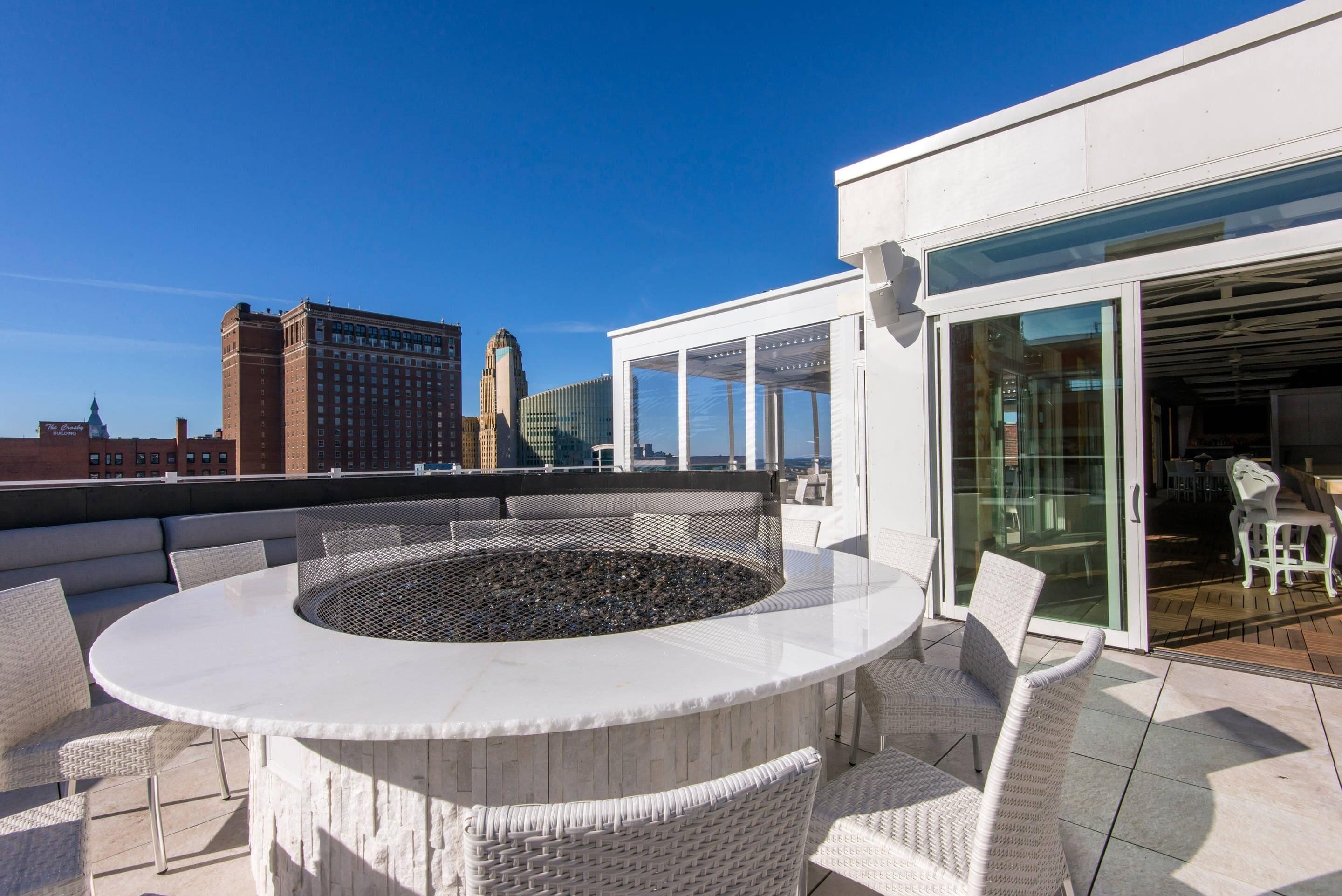 A rooftop terrace with a circular seating area, a glass door entrance, and a view of city buildings.