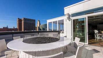 A rooftop terrace with a circular seating area, a glass door entrance, and a view of city buildings.