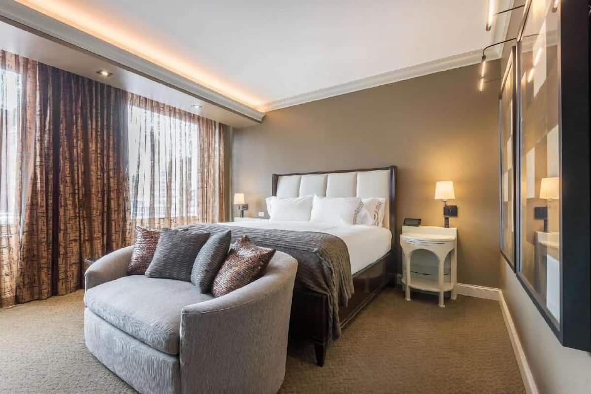 Una habitación de hotel con una cama, una silla, una mesita de noche y un ventanal con cortinas.