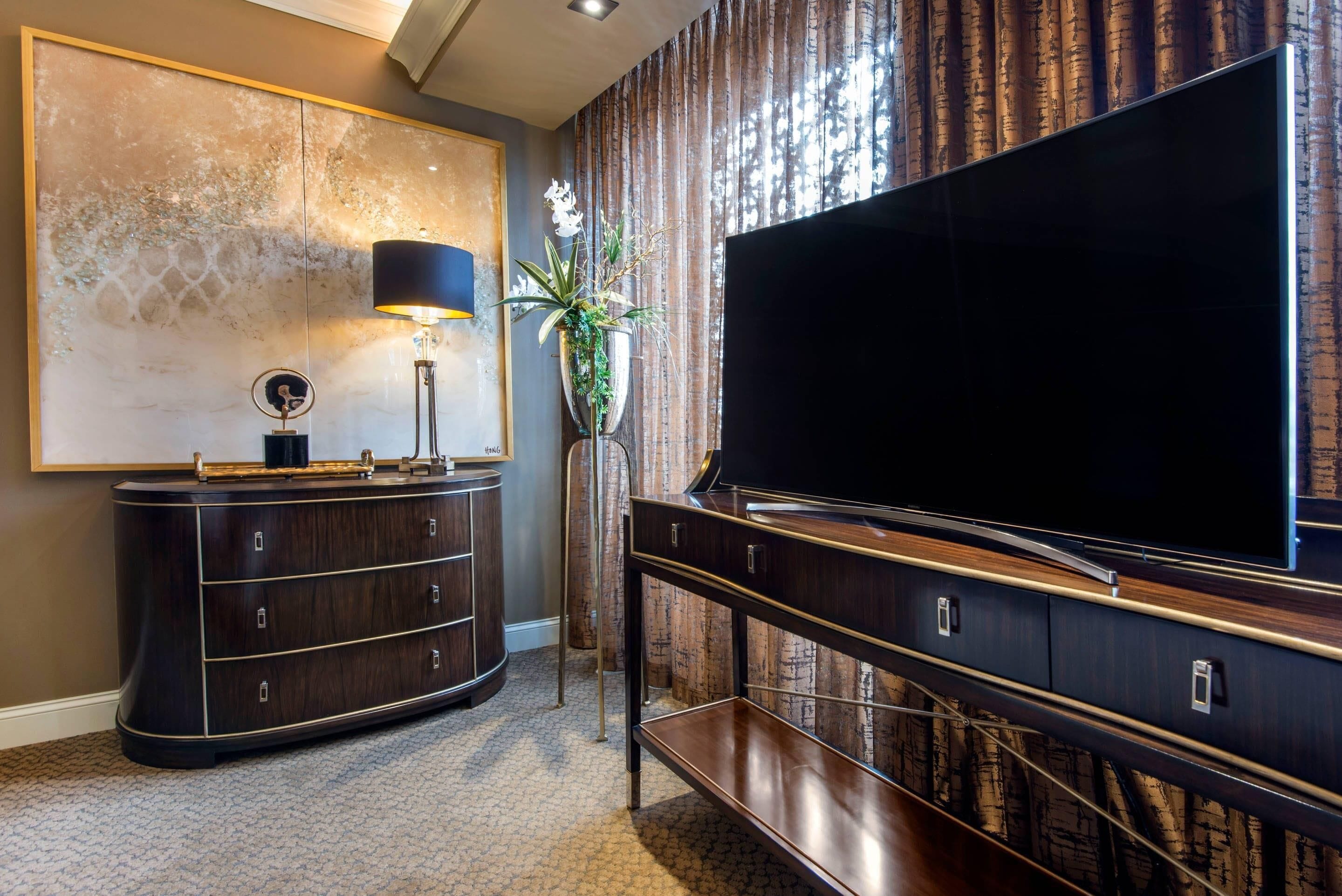 Un moderno salón con un televisor de pantalla plana grande, muebles de madera oscura, una lámpara decorativa y un cuadro abstracto grande en la pared.