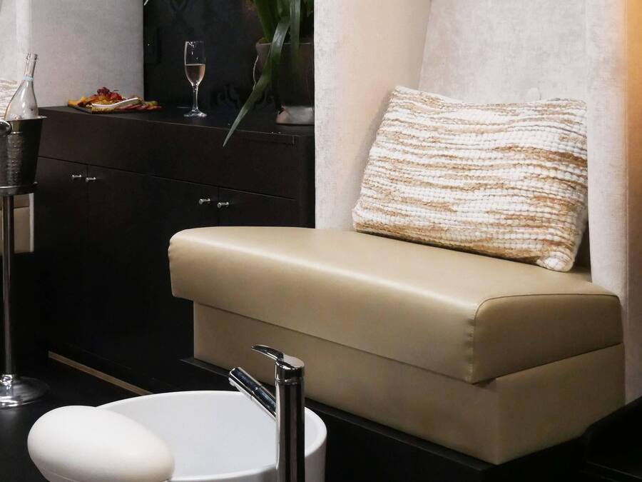 Un baño moderno con un sofá color beige, un lavamanos blanco, una copa de vino y una botella de agua sobre un mueble oscuro.