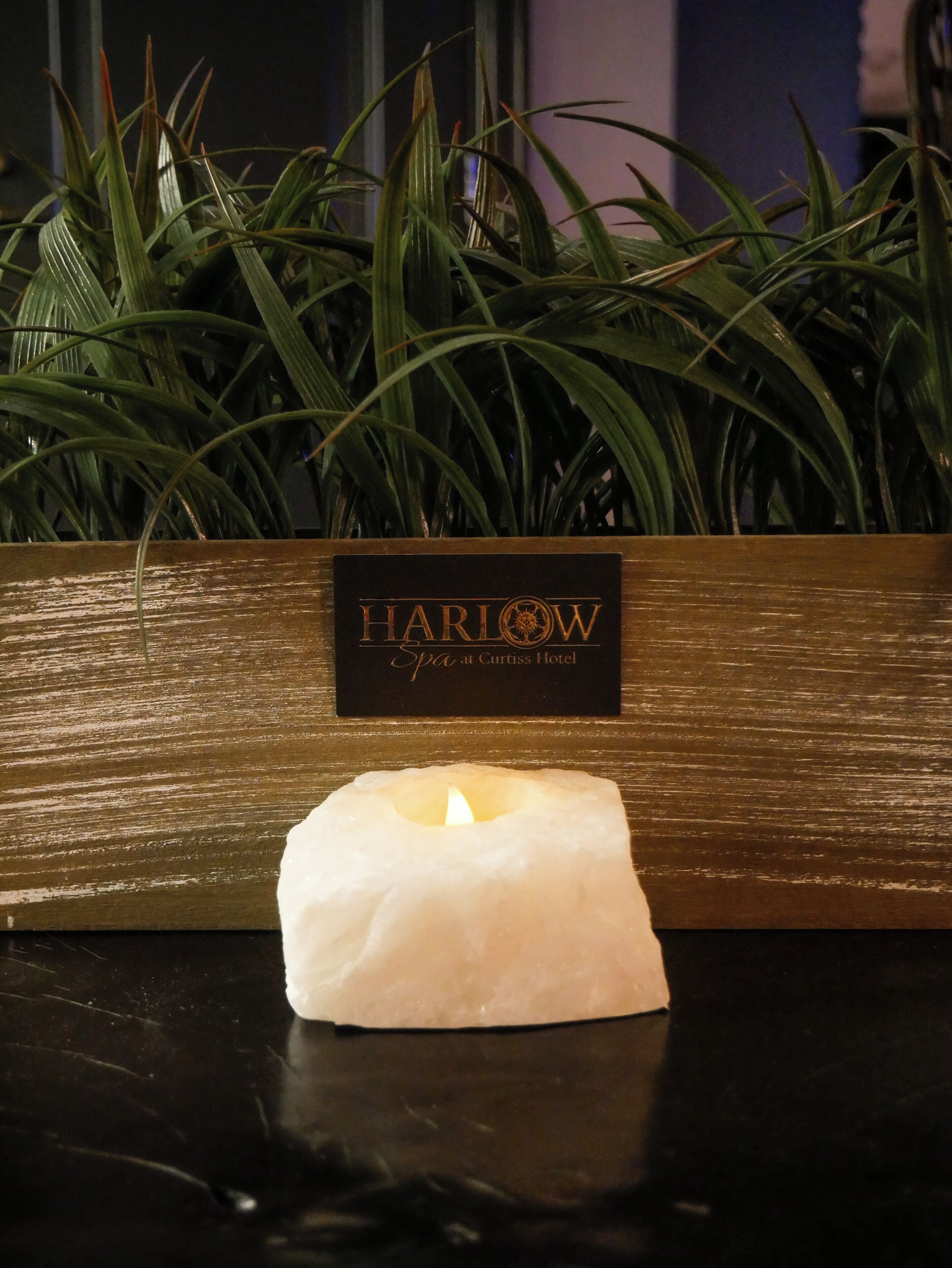 Eine Kerze auf einem Tisch mit einem Schild, das "Harlow Spa im Curtiss Hotel" zeigt.