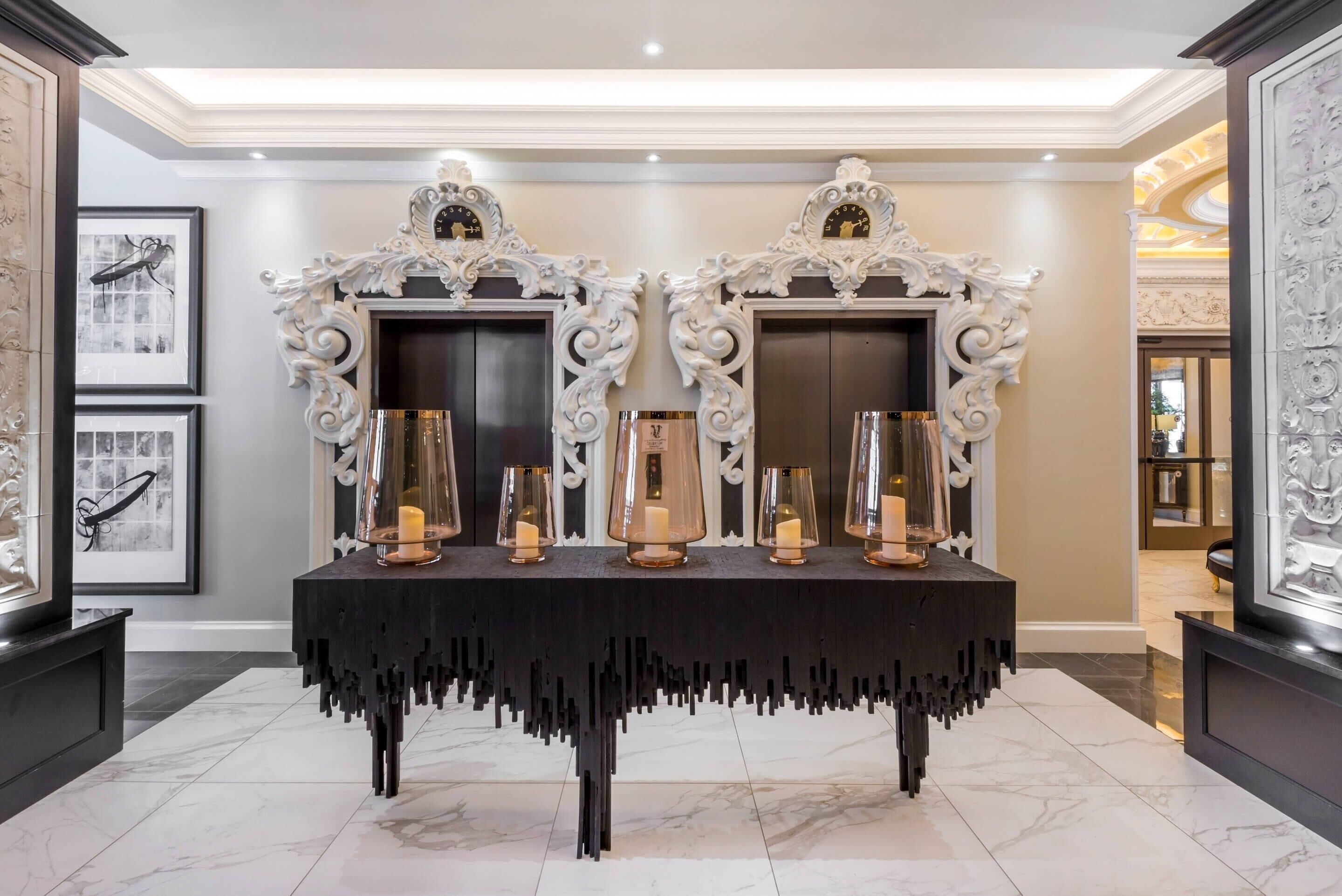 A luxurious lobby with a marble floor, ornate white wall decorations, and a central table with candles and glass candle holders.