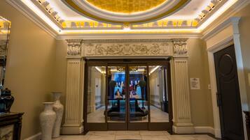A grand lobby with a large circular mosaic floor, a high ceiling with ornate decorations, and a glass door entrance.