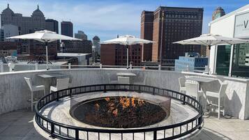 A rooftop terrace with a circular fire pit, outdoor seating, and a cityscape view.