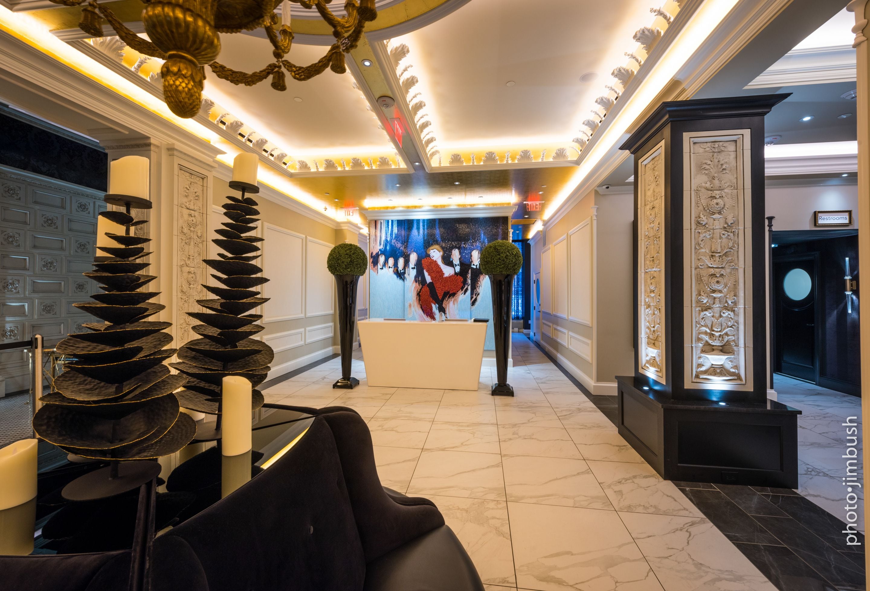 A lobby with a reception desk, a chandelier, and a decorative wall with a painting.