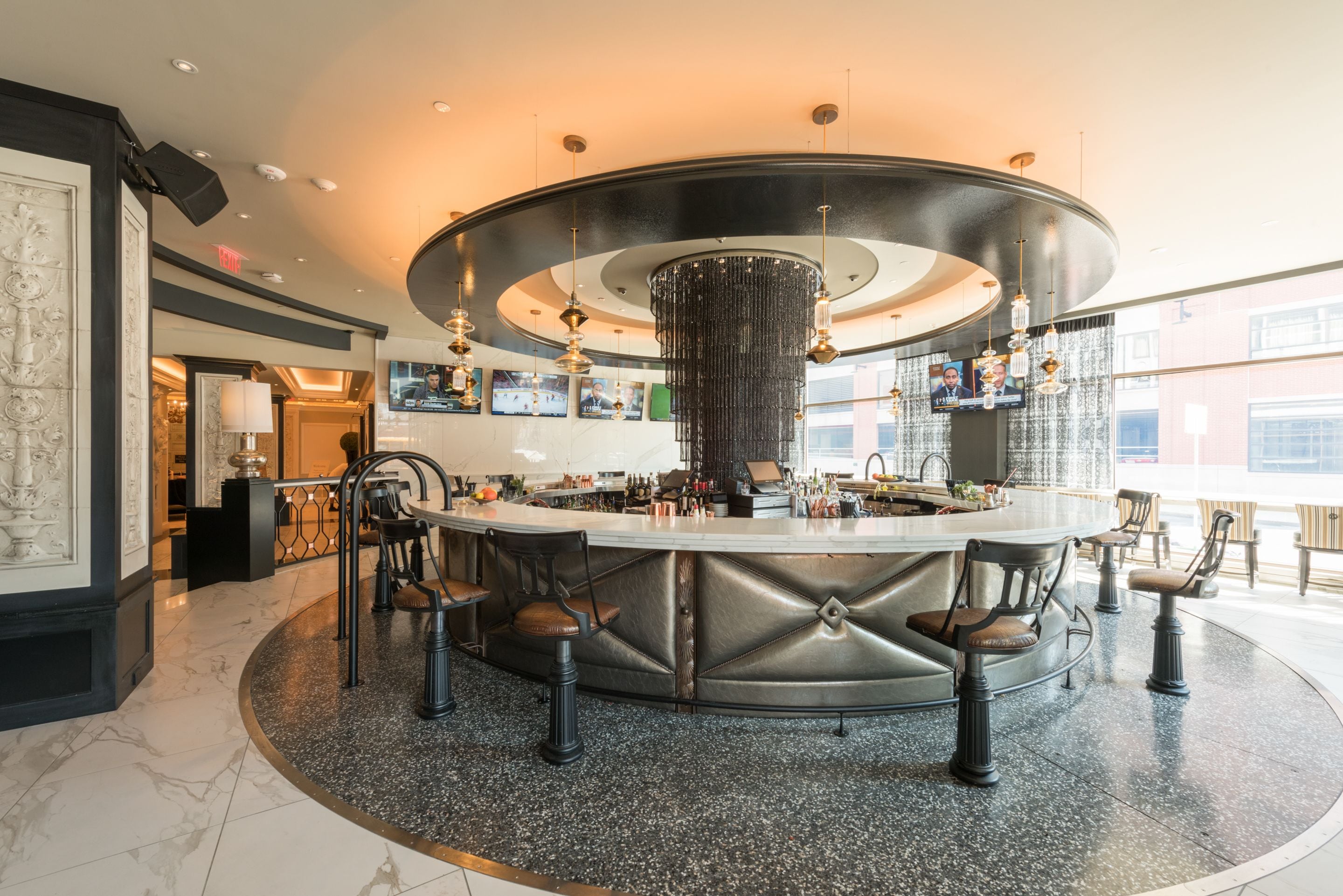 A circular bar area with a central chandelier, multiple TVs, and seating.
