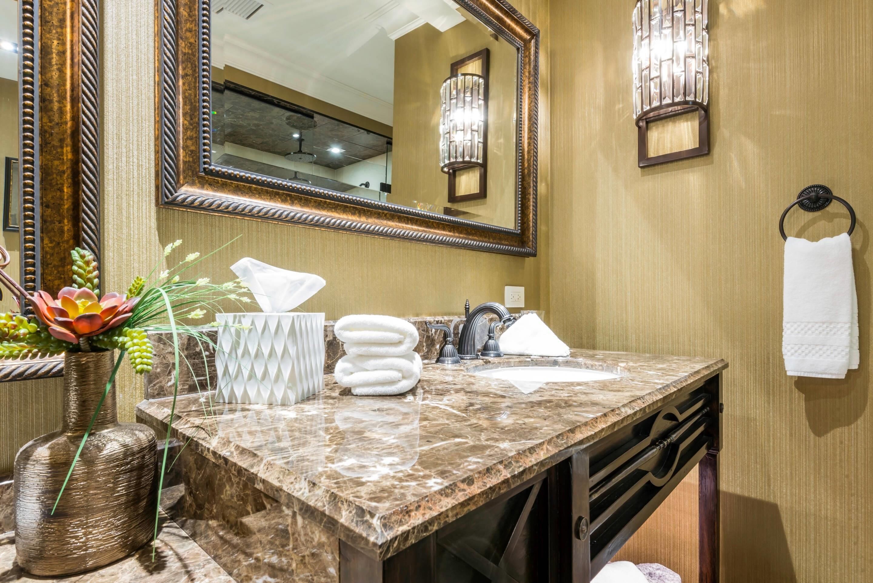 A bathroom with a marble sink, a large mirror, a towel rack, and a wall-mounted light fixture.