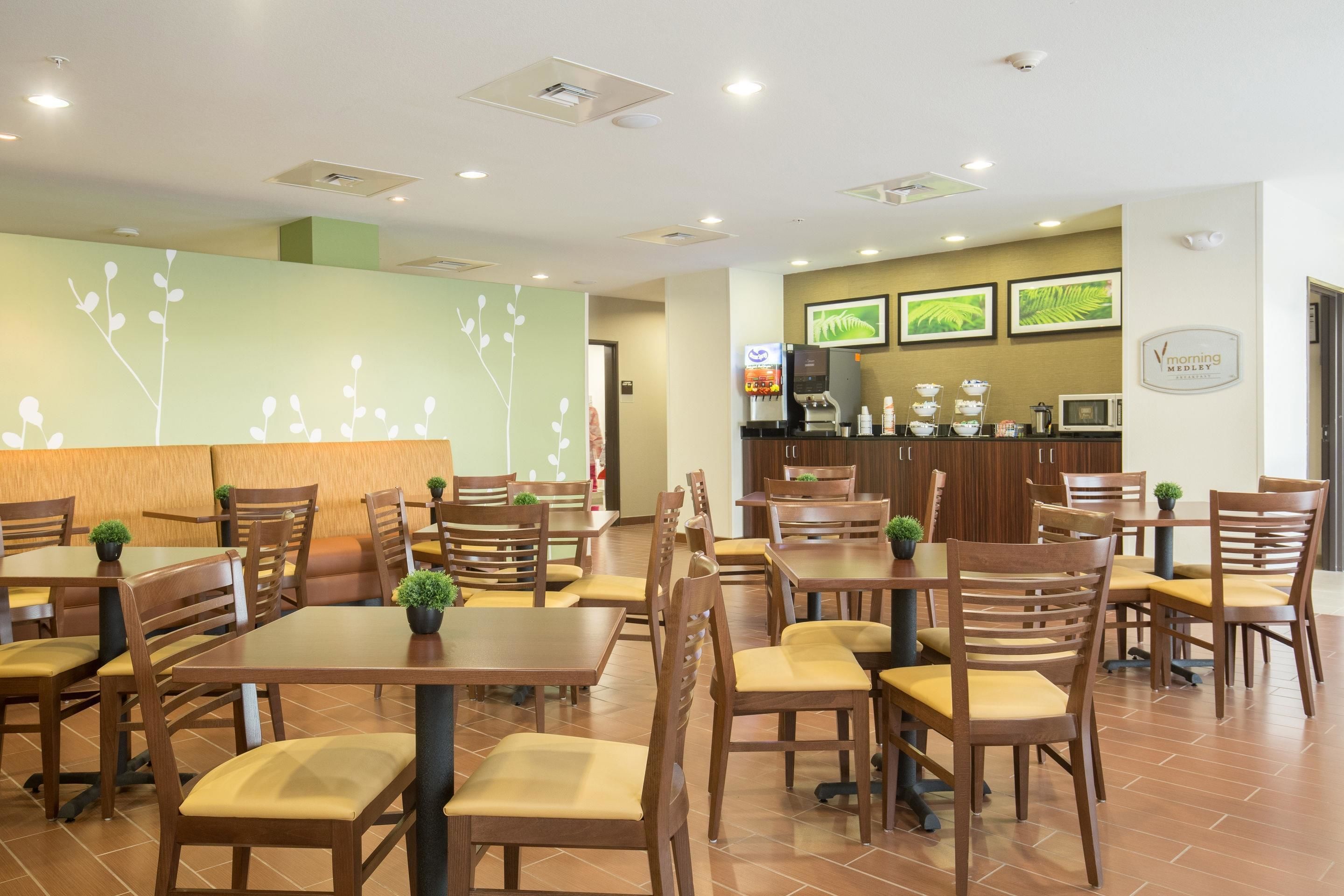 Un restaurante con mesas y sillas de madera, una barra con una máquina de café y una pared decorada con cuadros.