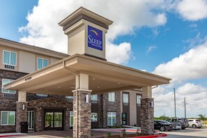A Sleep Inn & Suites building with a covered entrance, stone facade, and a parking lot with cars.