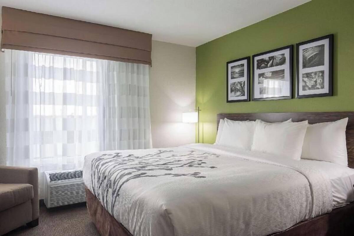 A hotel room with a bed, a chair, a heater, and three framed pictures on the wall.