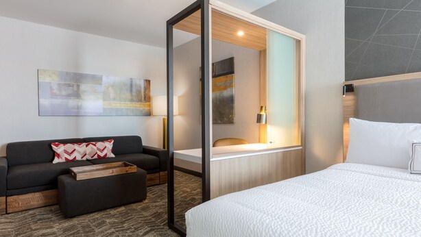 A modern hotel room with a large bed, a sofa, a wooden side table, and abstract artwork on the wall. - SpringHill Suites by Marriott Columbia (Columbia)