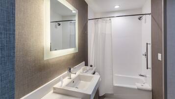 A modern bathroom with a large mirror, two sinks, a bathtub, and a shower curtain.