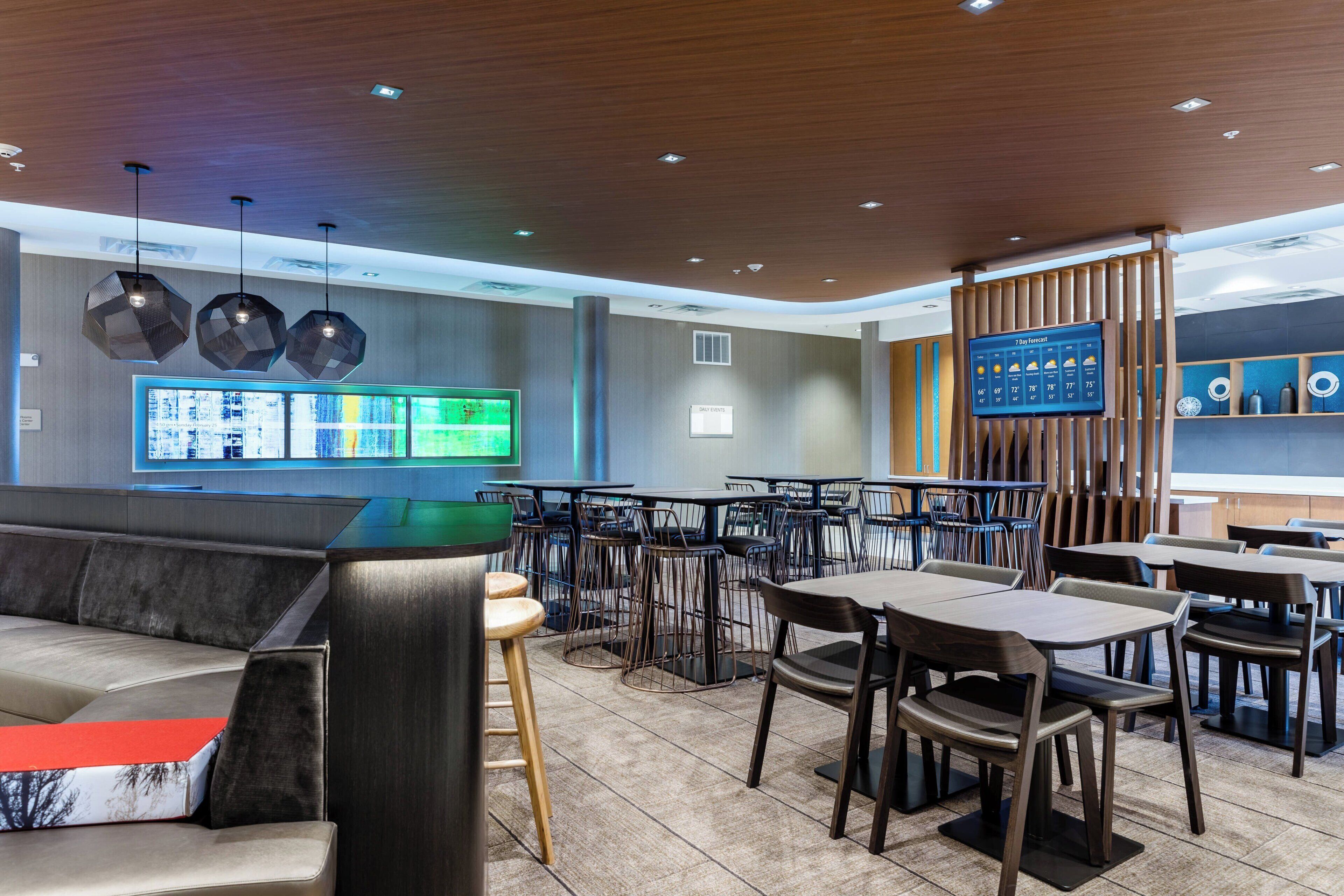 Un restaurante moderno con diversas opciones de asientos, como cabinas y mesas, un amplio menú digital y techo de madera.