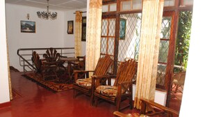 A room with wooden furniture, including chairs and a table, a red carpet, and a window with a view of greenery. - Kandy Shady Trees Villa (Kandy)