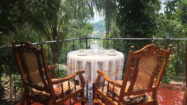 A round table with a floral tablecloth and matching chairs, set on a balcony with a view of lush greenery and a distant building. - Kandy Shady Trees Villa (Kandy)
