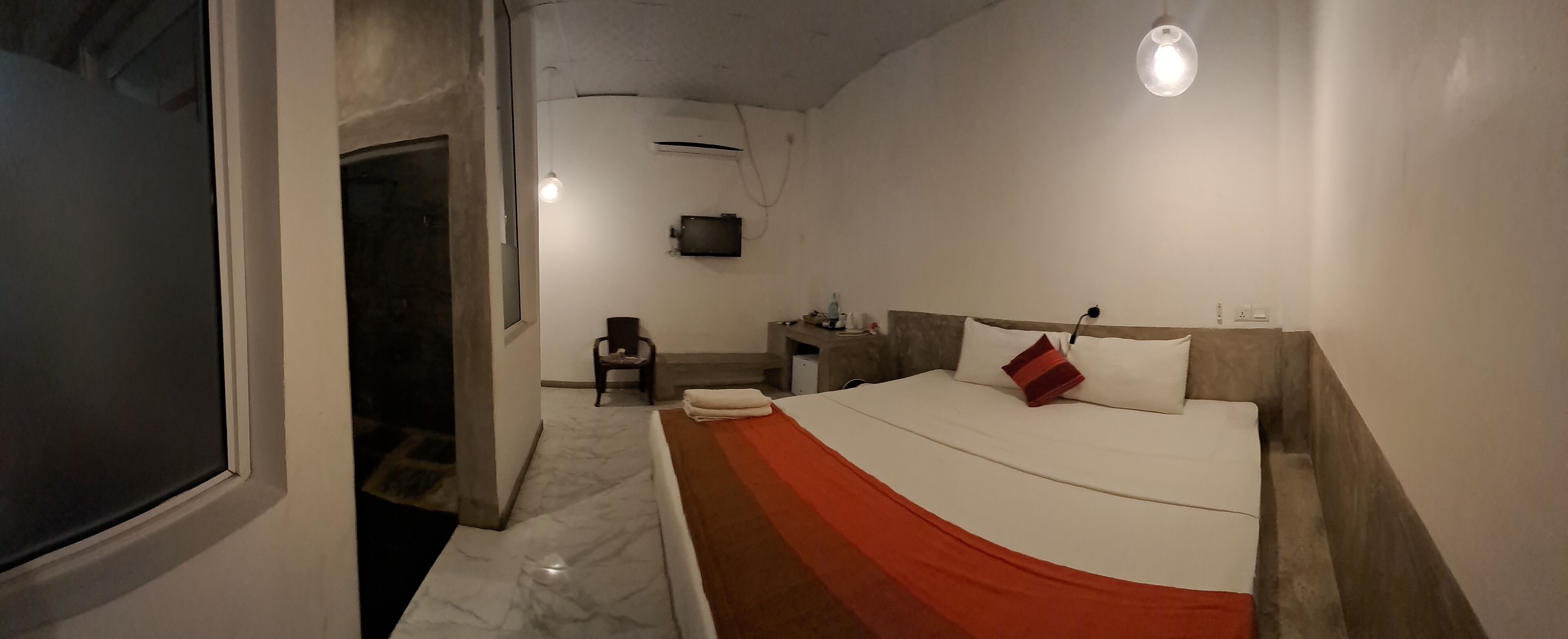 Quarto de hotel com uma cama, uma cadeira, uma escrivaninha e uma televisão.