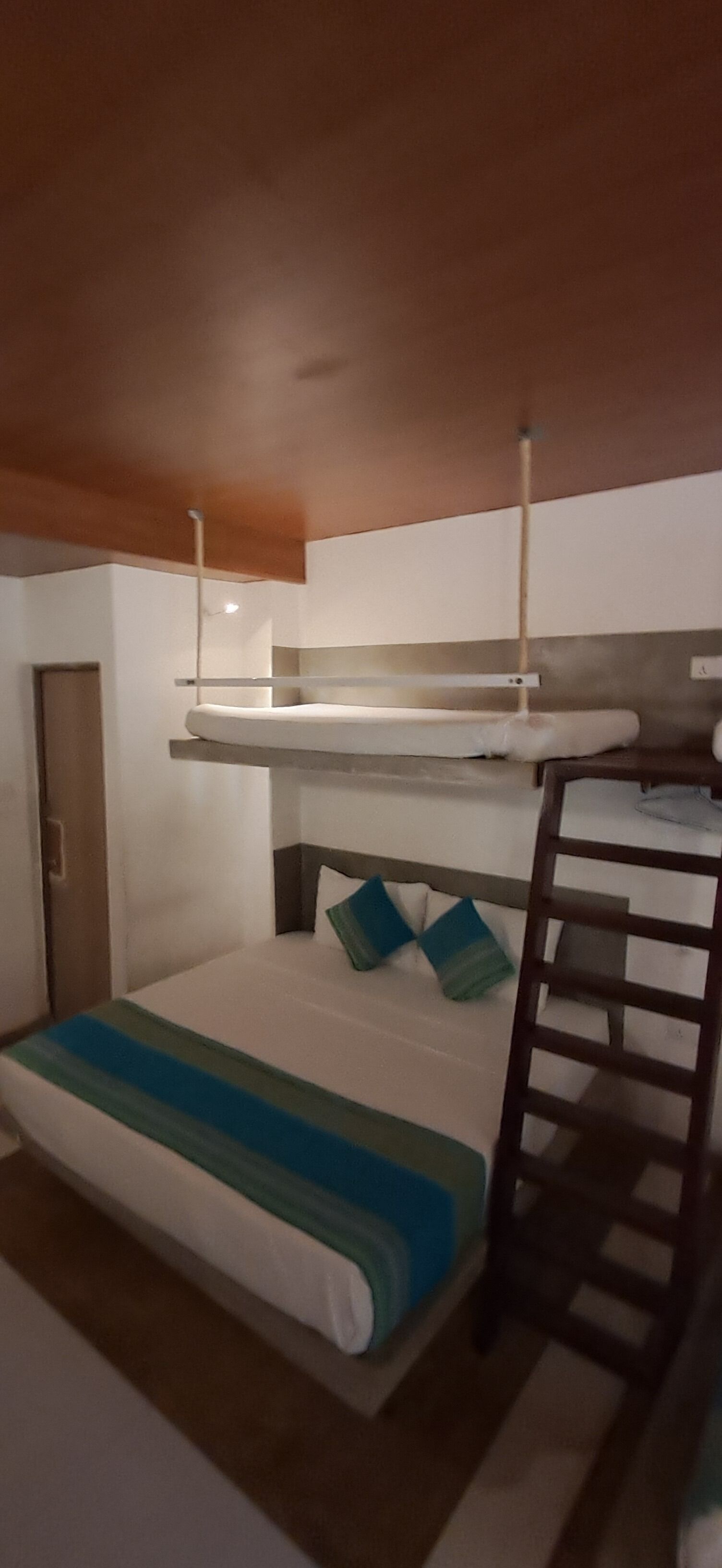 Una habitación pequeña y funcional con una cama litera, una escalera y una cama individual con un edredón a rayas.