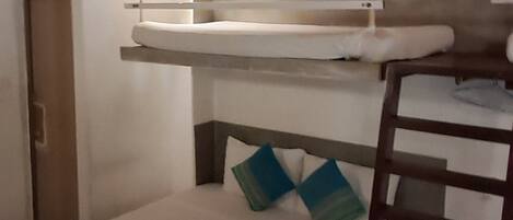 Una habitación pequeña y funcional con una cama litera, una escalera y una cama individual con un edredón a rayas.