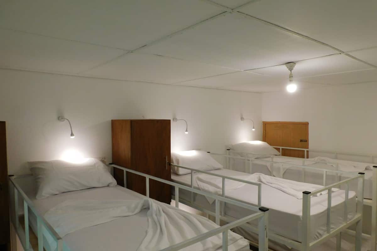 Une chambre avec trois lits superposés, chacun doté d’une tête de lit en bois et de draps blancs. Des lampes murales sont fixées au-dessus de chaque lit.