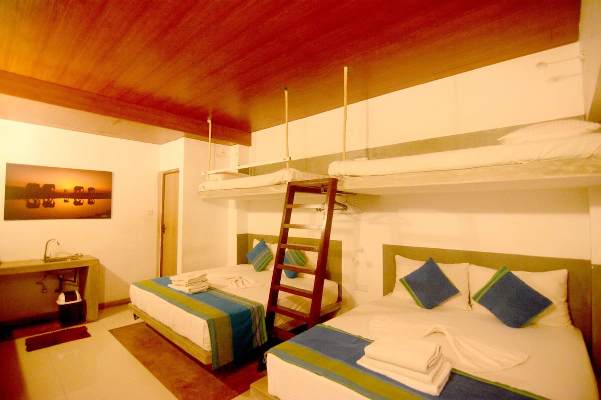 Une chambre d’hôtel avec des lits superposés, une échelle en bois, un bureau avec une chaise et un tableau accroché au mur.