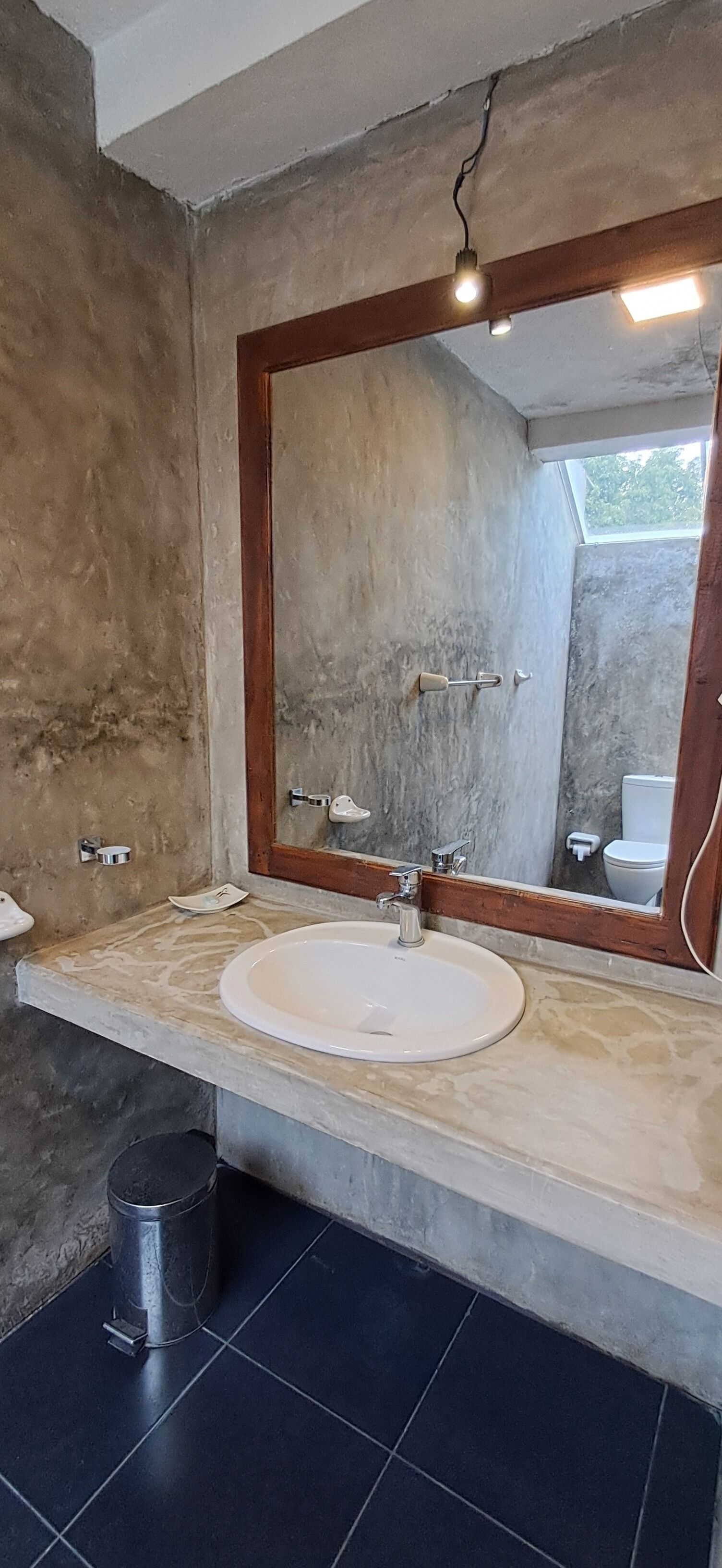 A bathroom with a large mirror, a sink, and a trash can.