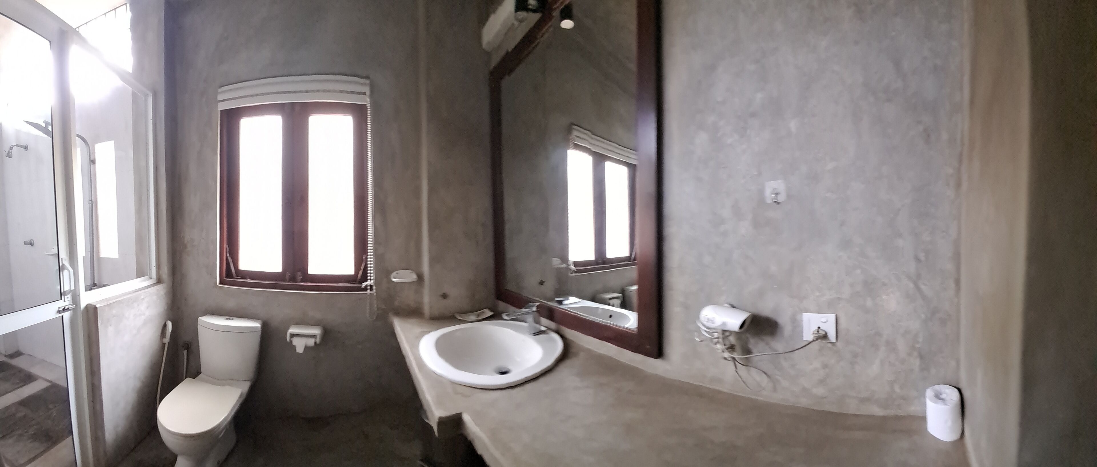 A bathroom with a toilet, sink, mirror, and a window.