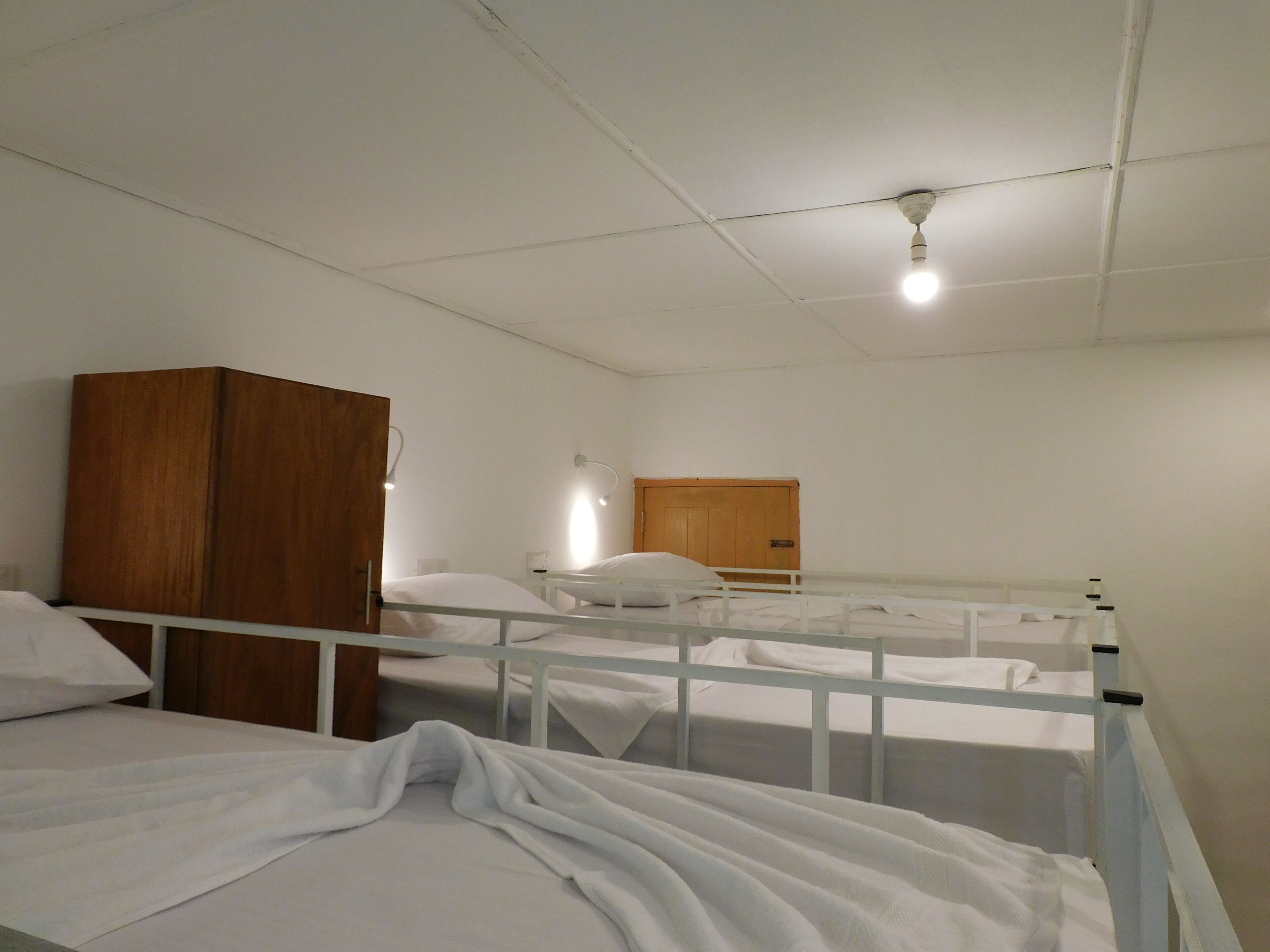 Une chambre de dortoir avec des lits superposés, une armoire en bois et un luminaire au plafond.