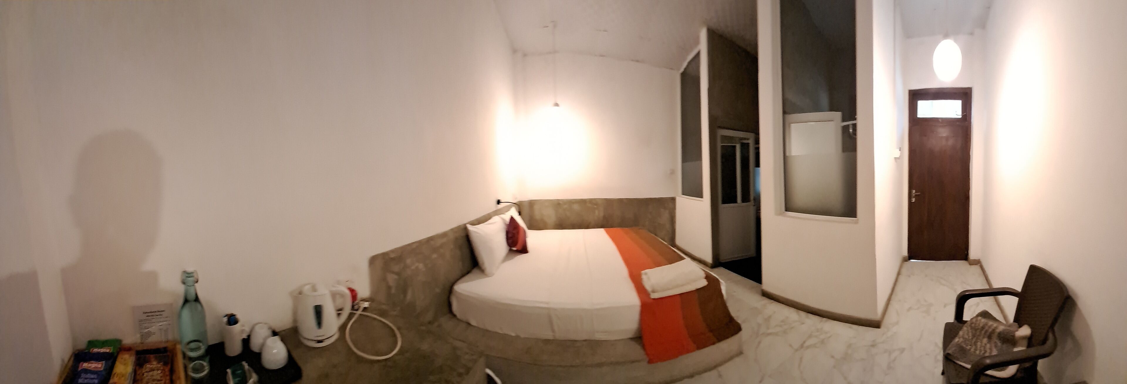 Een kleine, compacte hotelkamer met een enkel bed, een stoel en een kitchenette.