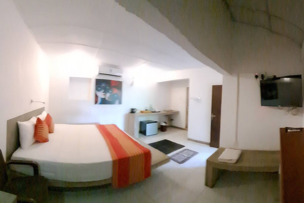 Une chambre d’hôtel avec un lit, un bureau, une chaise, une télévision et une salle de bain visible au fond.
