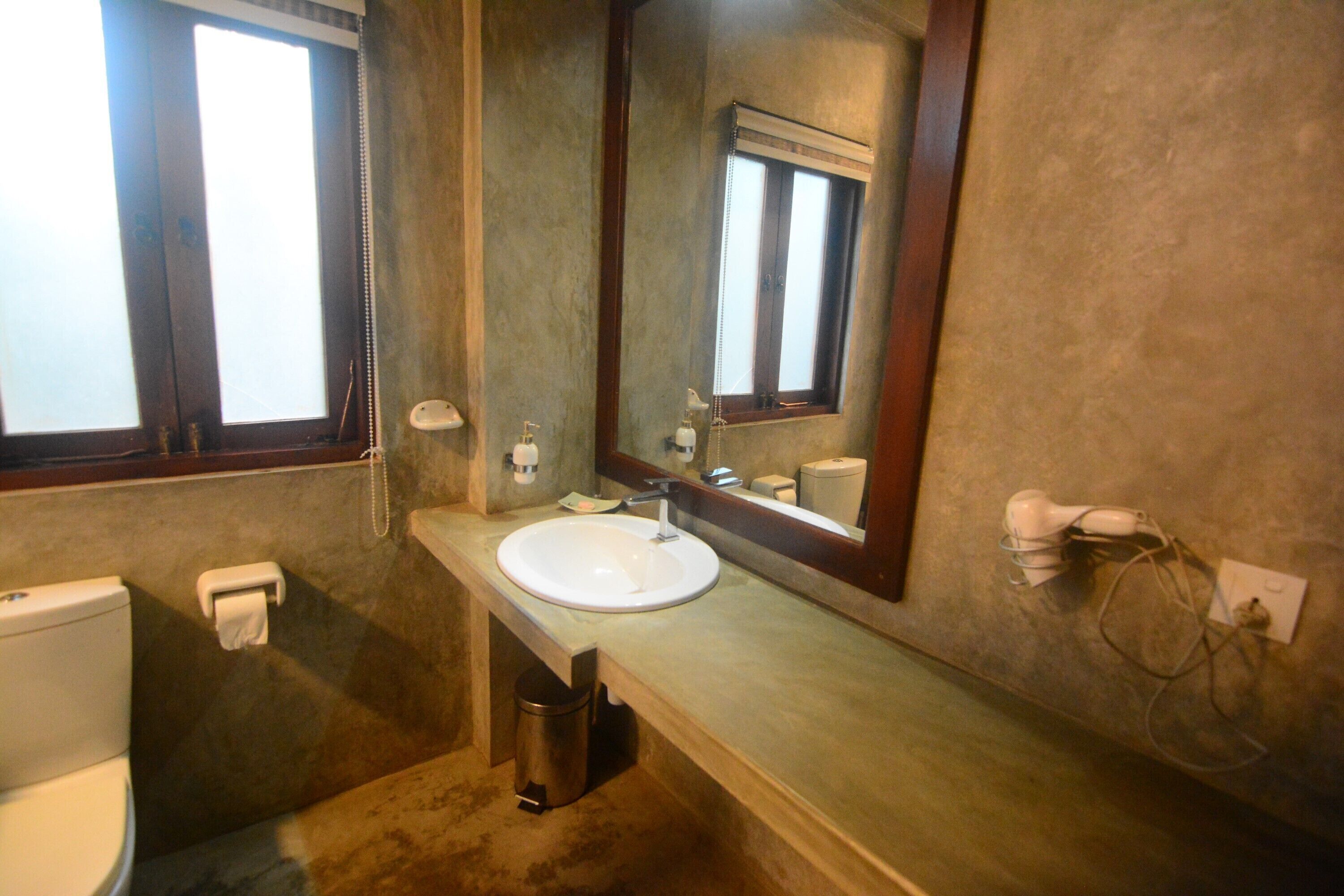 Ein Badezimmer mit einem weißen Waschbecken, einem Spiegel, einer Toilette und einem Mülleimer.