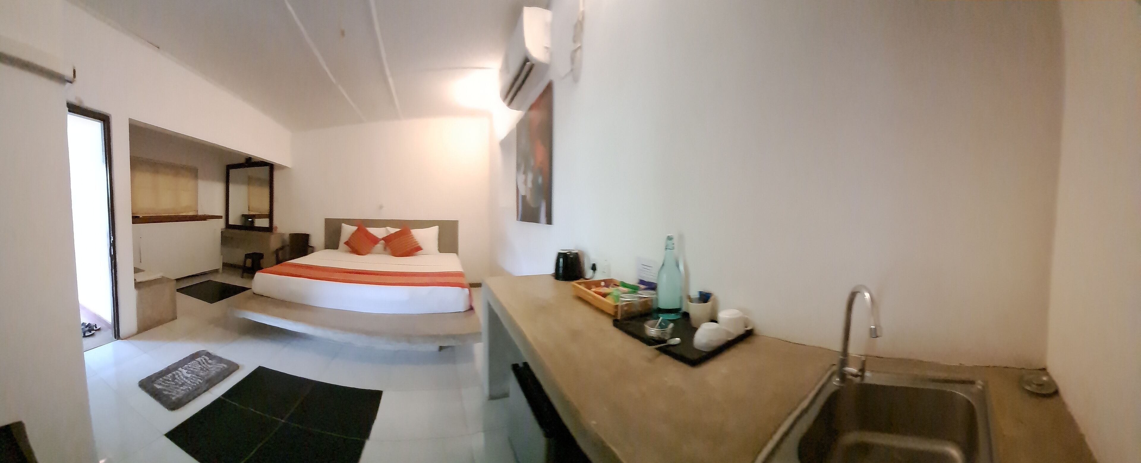 Een kleine hotelkamer met een bed, een kitchenette, een spoelbak en een raam.