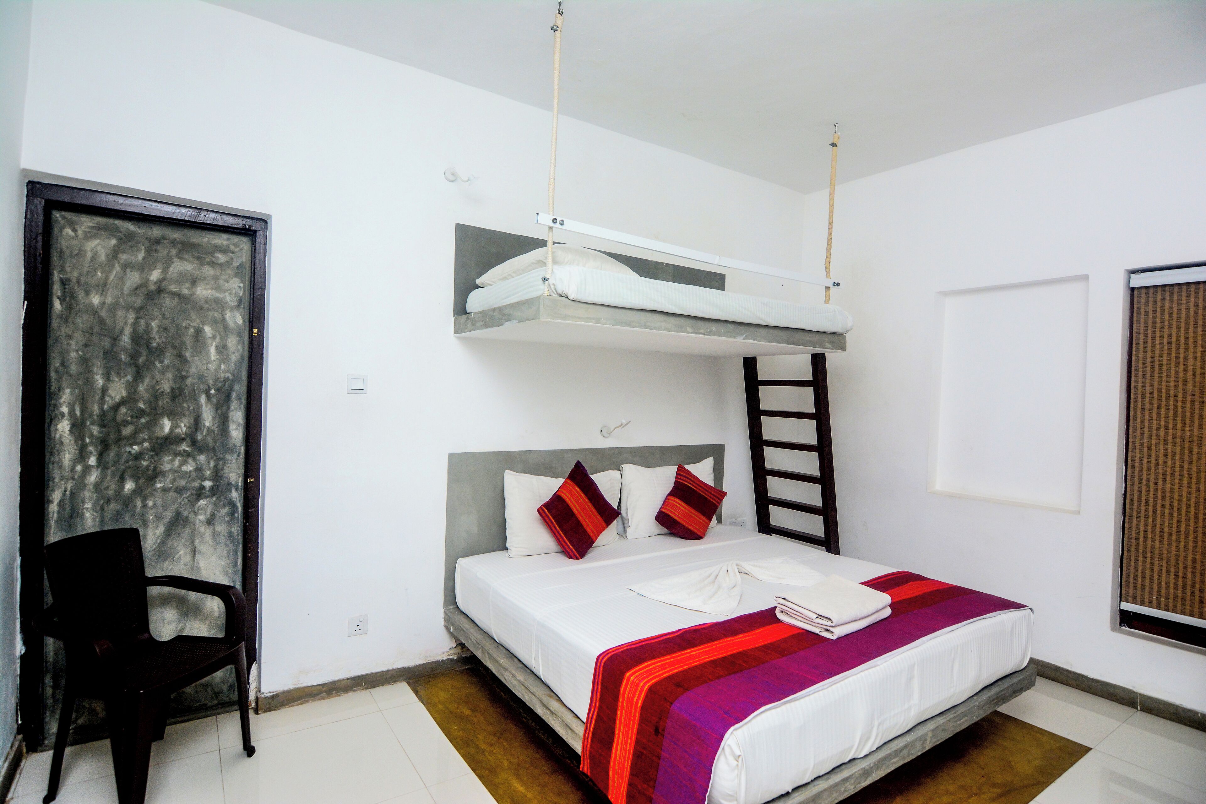 Una habitación con literas, una silla y un ventanal con persianas.