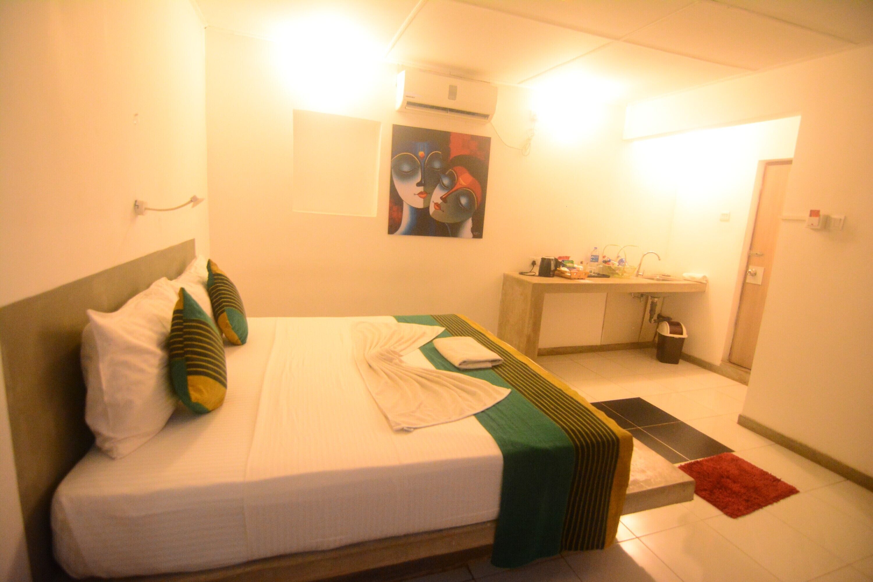 Hotelkamer met een bed, kussens, een nachtkastje, een spiegel, een wastafel en een rood vloerkleed.