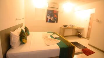 A hotel room with a bed, pillows, a bedside table, a mirror, a sink, and a red rug.