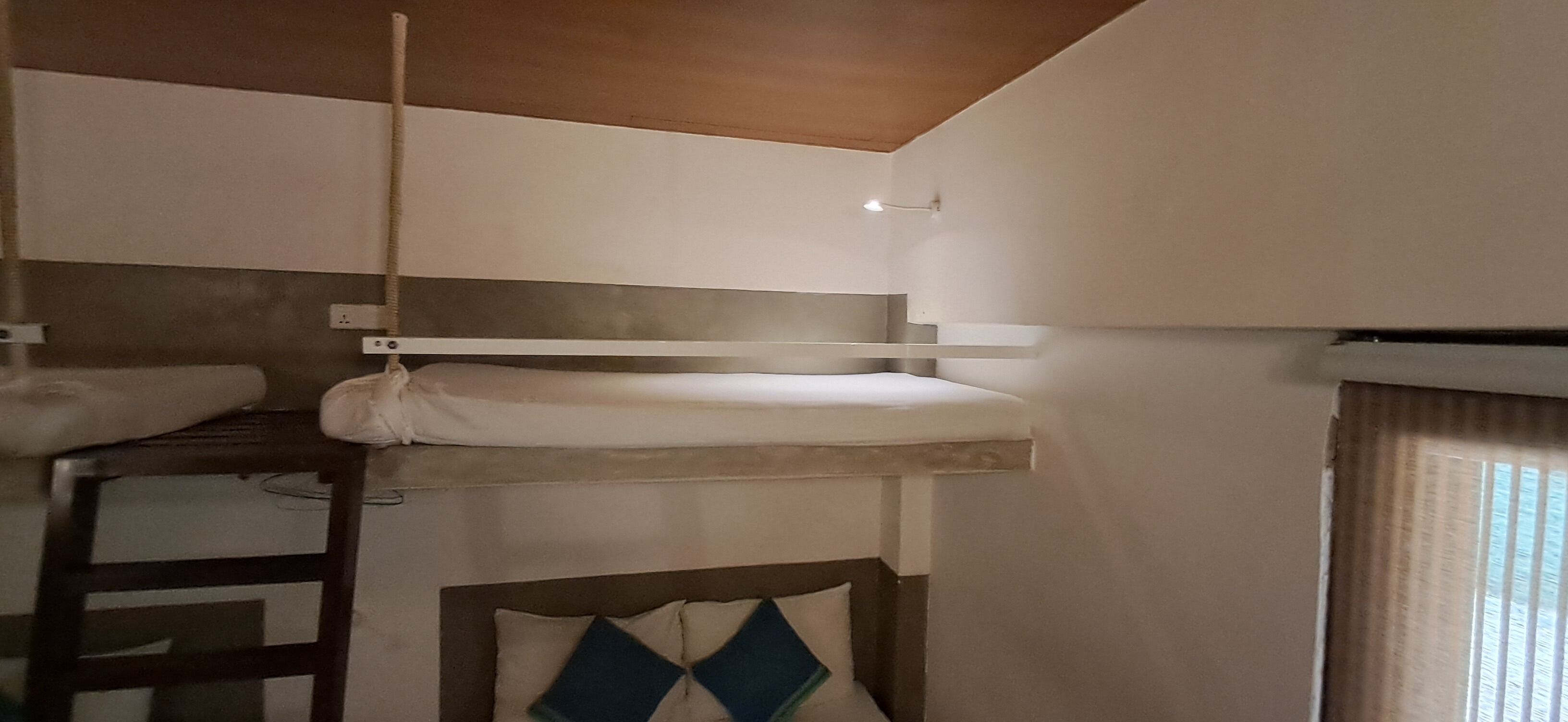 Una cama litera con una escalera, un cabecero con un cojín decorativo y una ventana con cortinas.
