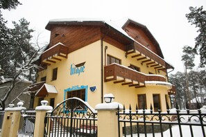 A two-story building with a yellow facade, wooden balconies, and a snow-covered roof. - Hotel Shale (Perm)