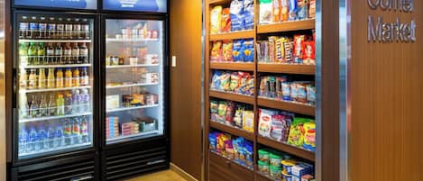 Un mercado de barrio con dispensadores refrigerados para bebidas y estantes llenos de aperitivos y productos básicos.
