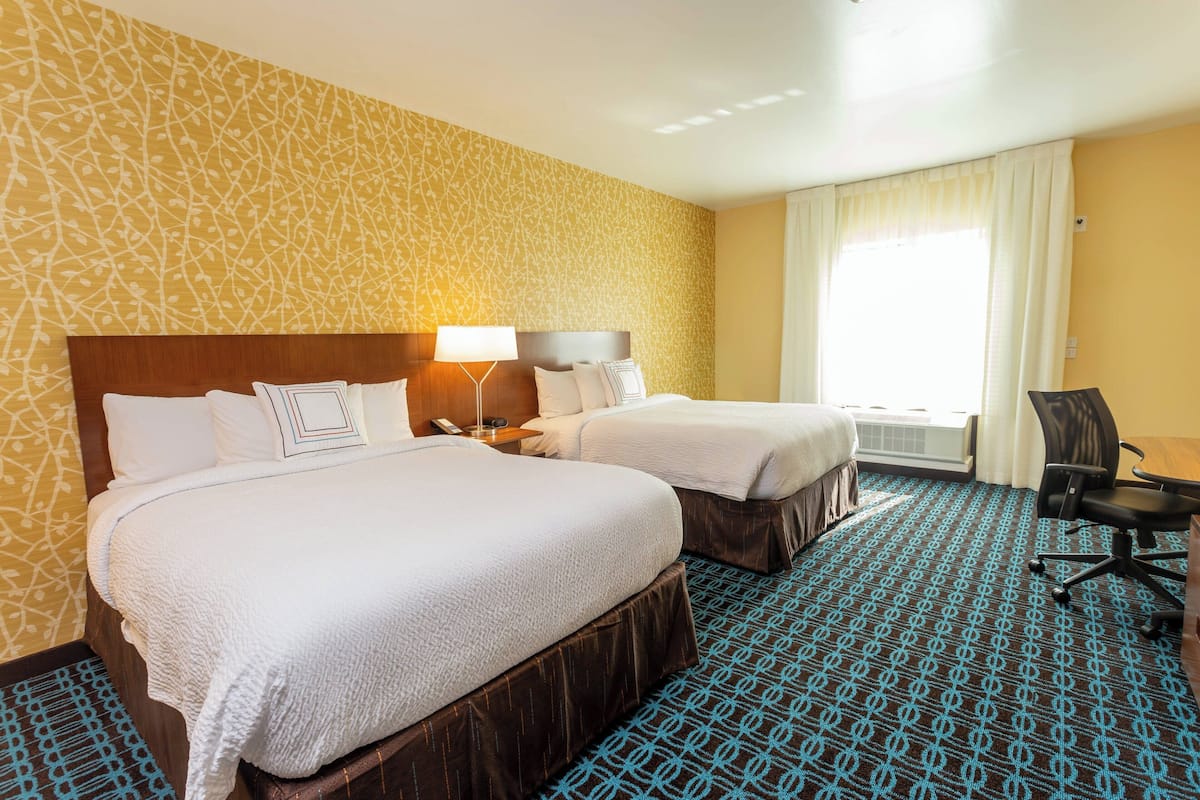 A hotel room with two beds, a desk, and a chair.