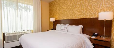 A hotel room with a large bed, two bedside tables, a wall-mounted lamp, and a window with sheer curtains.