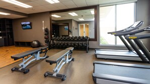 A gym with treadmills, a bench, dumbbells, and a television on the wall.