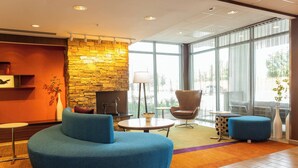 A modern lobby with a stone accent wall, a blue sofa, a round table, and a large window offering a view of the outdoors.