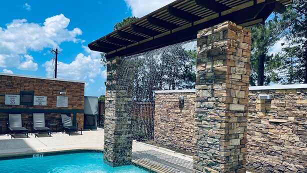 A pool area with stone pillars, lounge chairs, and a covered seating area.