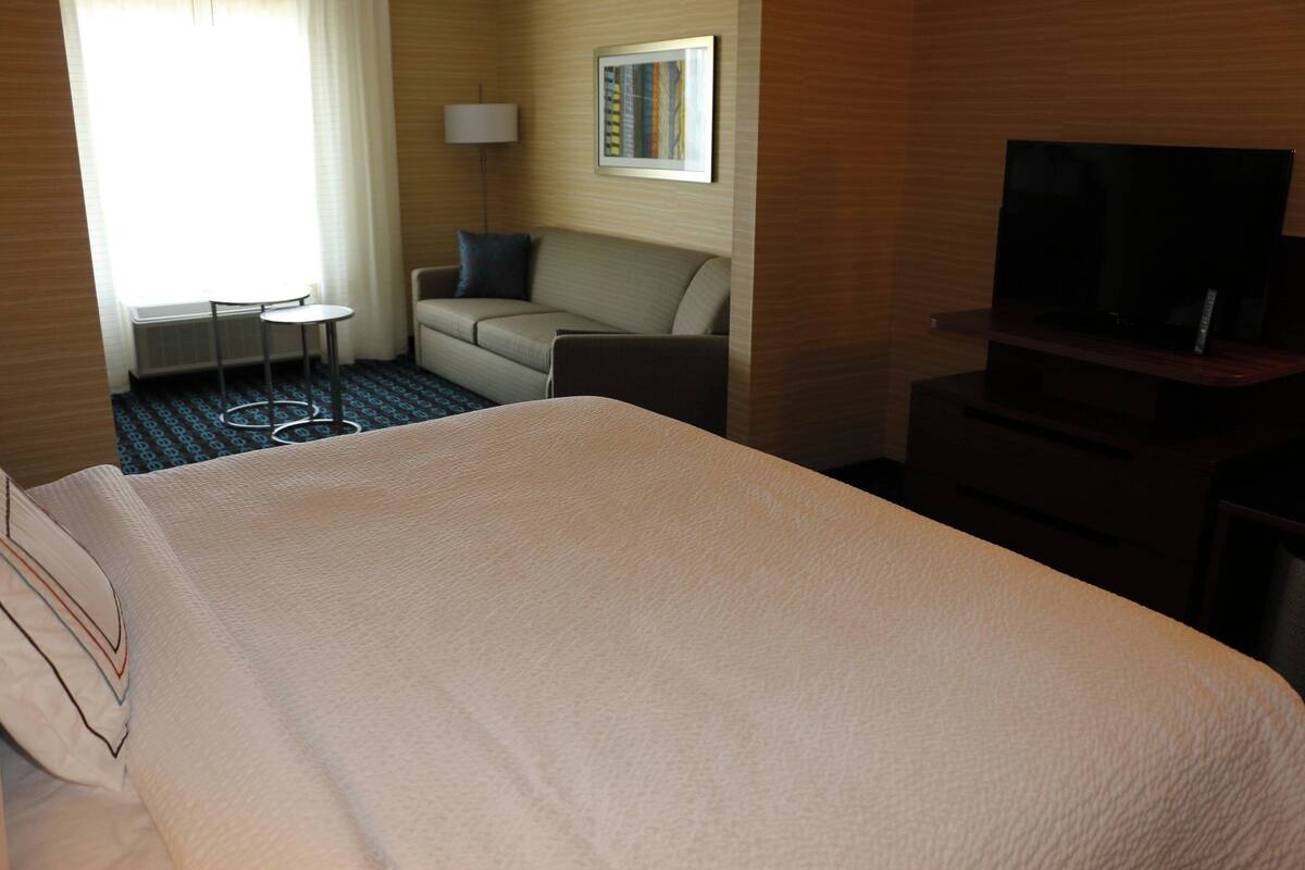 A hotel room with a large bed, a sofa, a small table, a TV, and a lamp.
