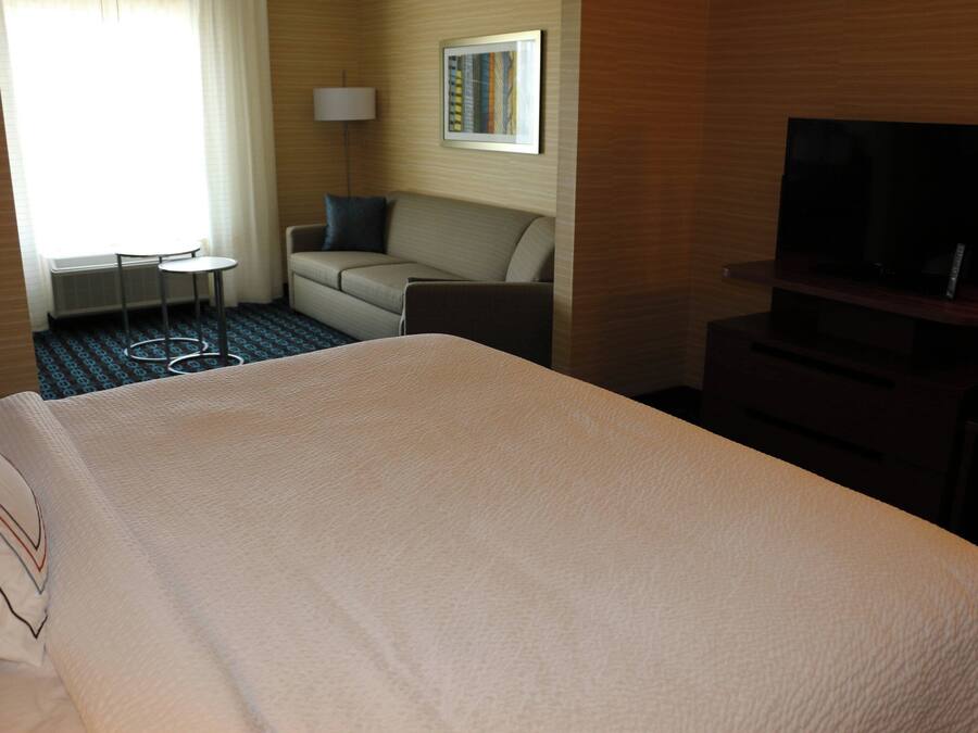 Una habitación de hotel con una cama grande, un sofá, una mesita, un televisor y una lámpara.