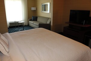 Una habitación de hotel con una cama grande, un sofá, una mesita, un televisor y una lámpara.