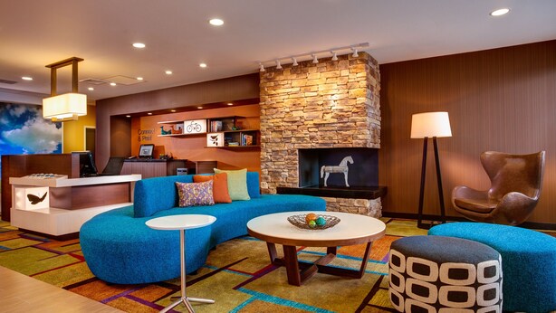 A modern living room with a stone fireplace, a blue sofa, a round coffee table, and a desk with a computer.