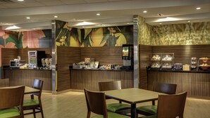 A restaurant with wooden paneling, a counter with food and drink options, and green cushioned chairs.