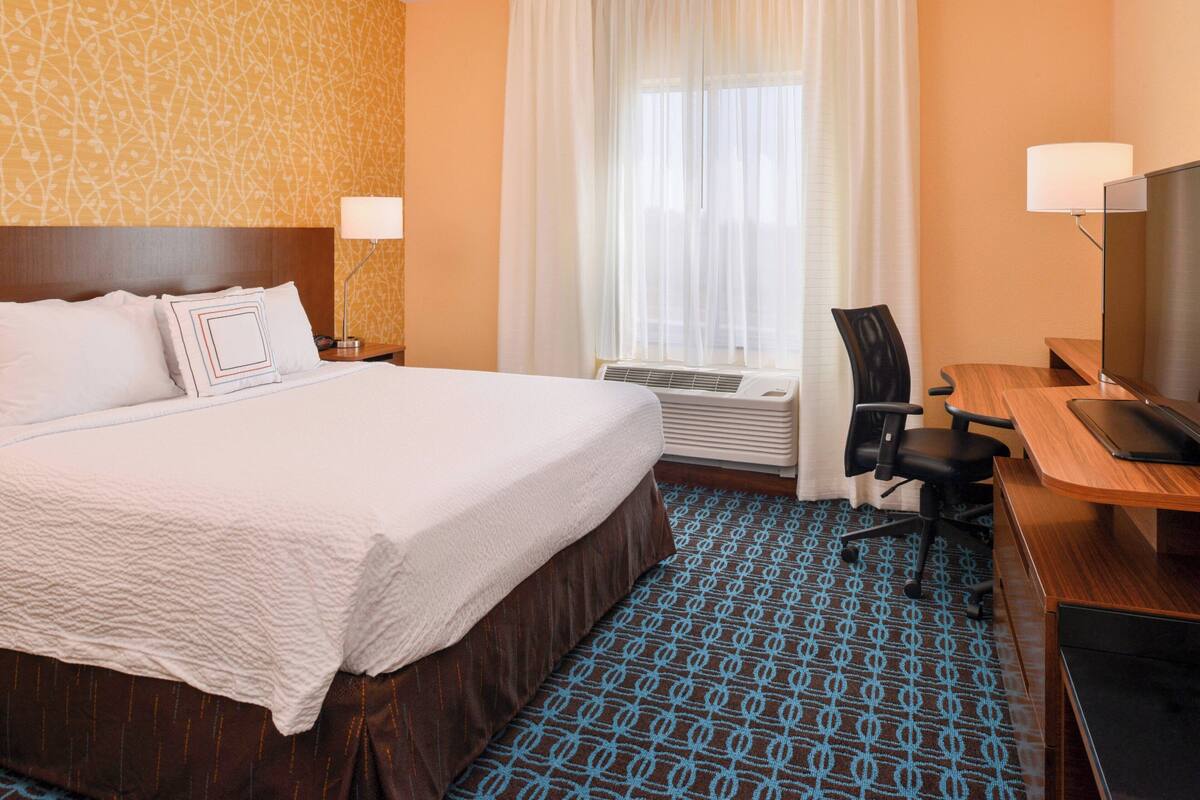 A hotel room with a large bed, a desk with a computer, a chair, and a TV.