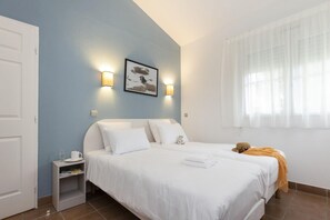 A hotel room with a bed, bedside table, and a window with sheer curtains.